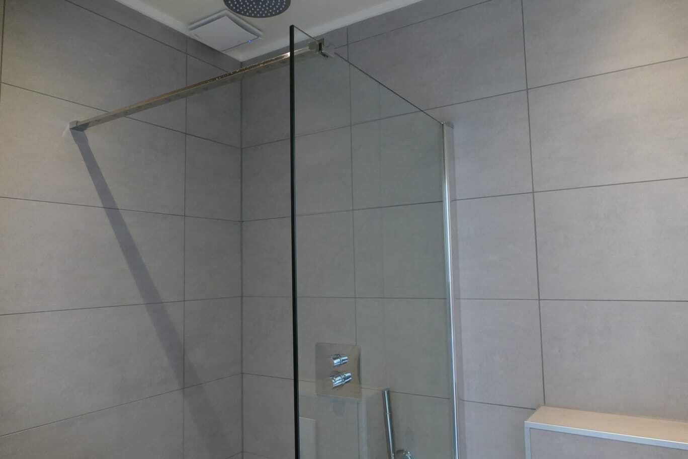 Een douchecabine met glazen wanden en deur, betegelde wanden en een plafondlamp.