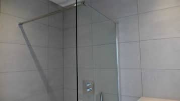 Een douchecabine met glazen wanden en deur, betegelde wanden en een plafondlamp.