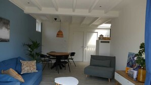 Una sala de estar moderna con un sofá azul, un sillón gris, una mesa de comedor redonda con sillas, una mesa de centro blanca y una lámpara colgante.