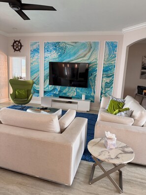 Ein modernes Wohnzimmer mit einem Flachbildfernseher, zwei Sofas, einem grünen Sessel und einem Marmortisch.