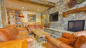 A cozy living room with leather sofas, a wooden coffee table, a stone fireplace, and a bookshelf filled with books. - River Run Village Walk To Gondola Pool Hot Tubs Restaurants and Shops DELUXE (Keystone)