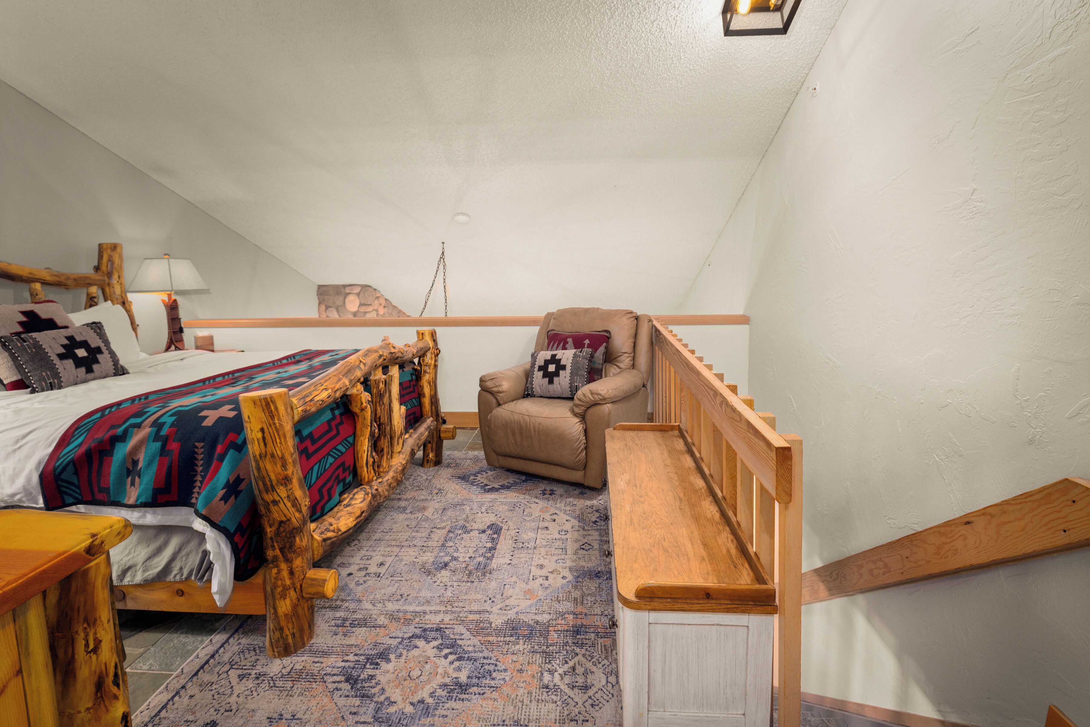 Ein Schlafzimmer mit einem Bett, einem Sessel, einer Holzbank, einer Lampe und einem Teppich.