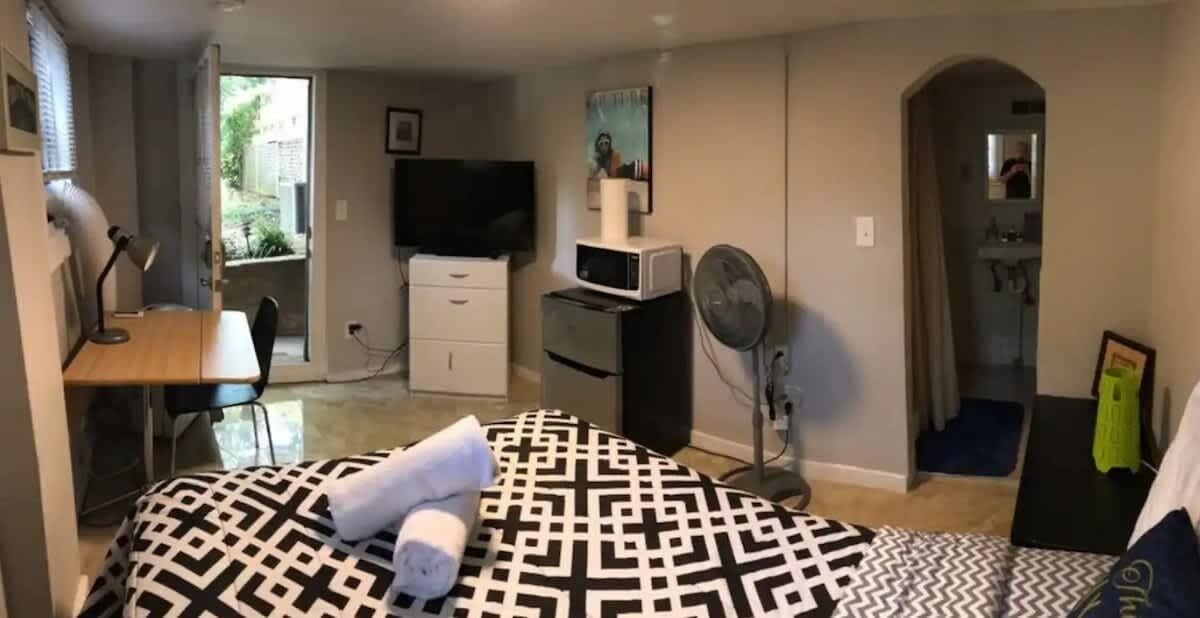 Een slaapkamer met een bed, bureau, stoel, televisie, magnetron en ventilator.
