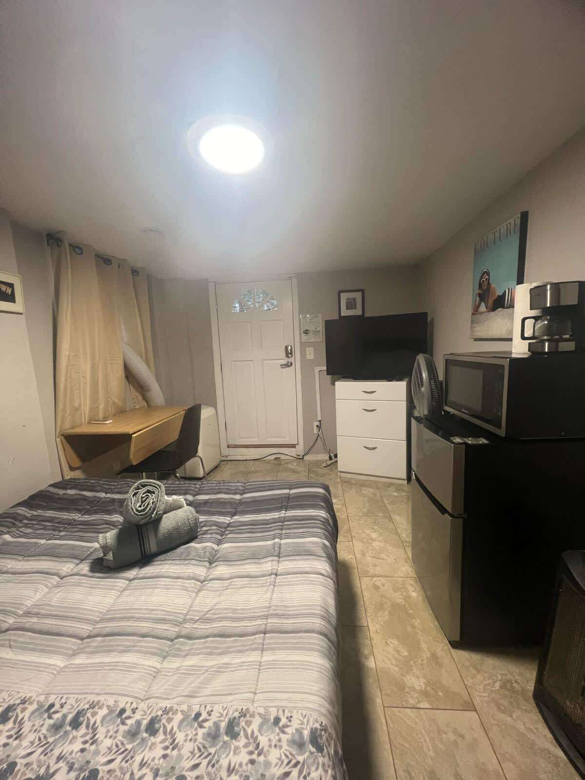 Habitación de hotel con cama, escritorio, televisión y kitchenette.