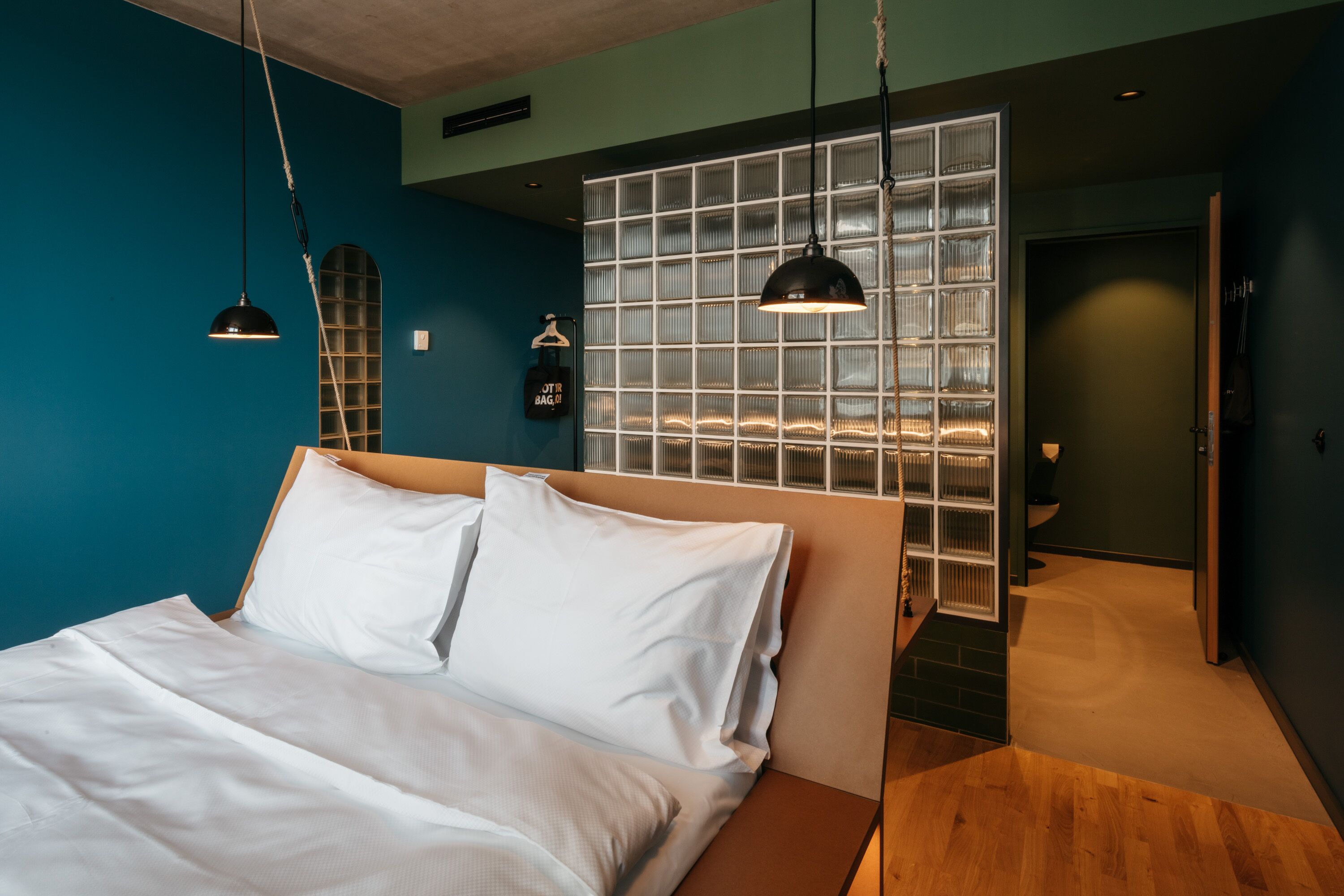 A modern bedroom with a large bed, a glass partition wall, and a wooden floor.