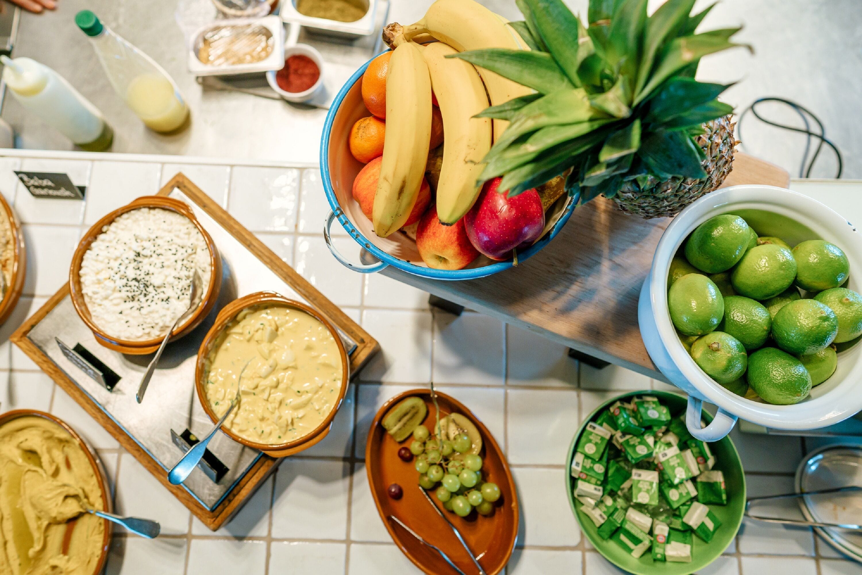 A buffet table with various food items including fruits, dips, and a bowl of green cubes.