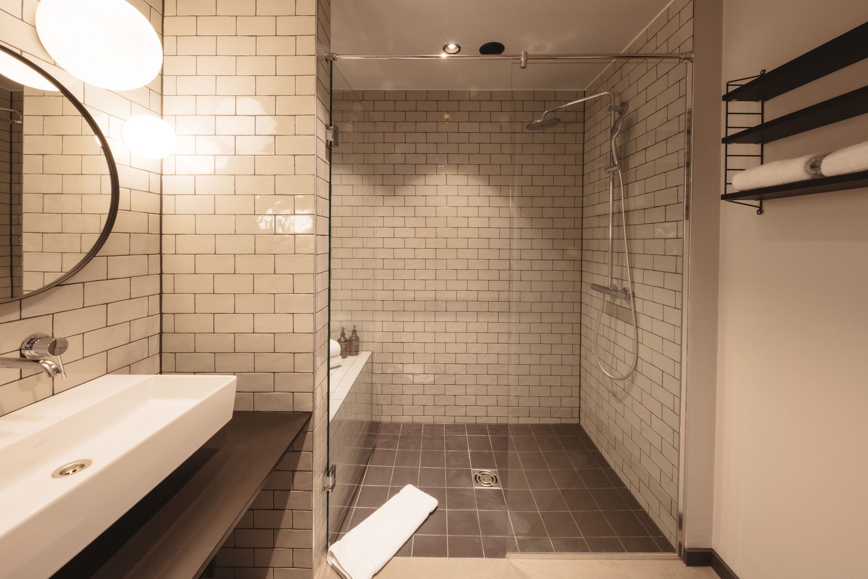Une salle de bain moderne avec une douche à parois de verre, un lavabo blanc et un miroir agrémenté de lumières rondes.