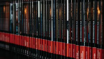 Una hilera de libros con lomos rojos y cubiertas negras en una estantería.