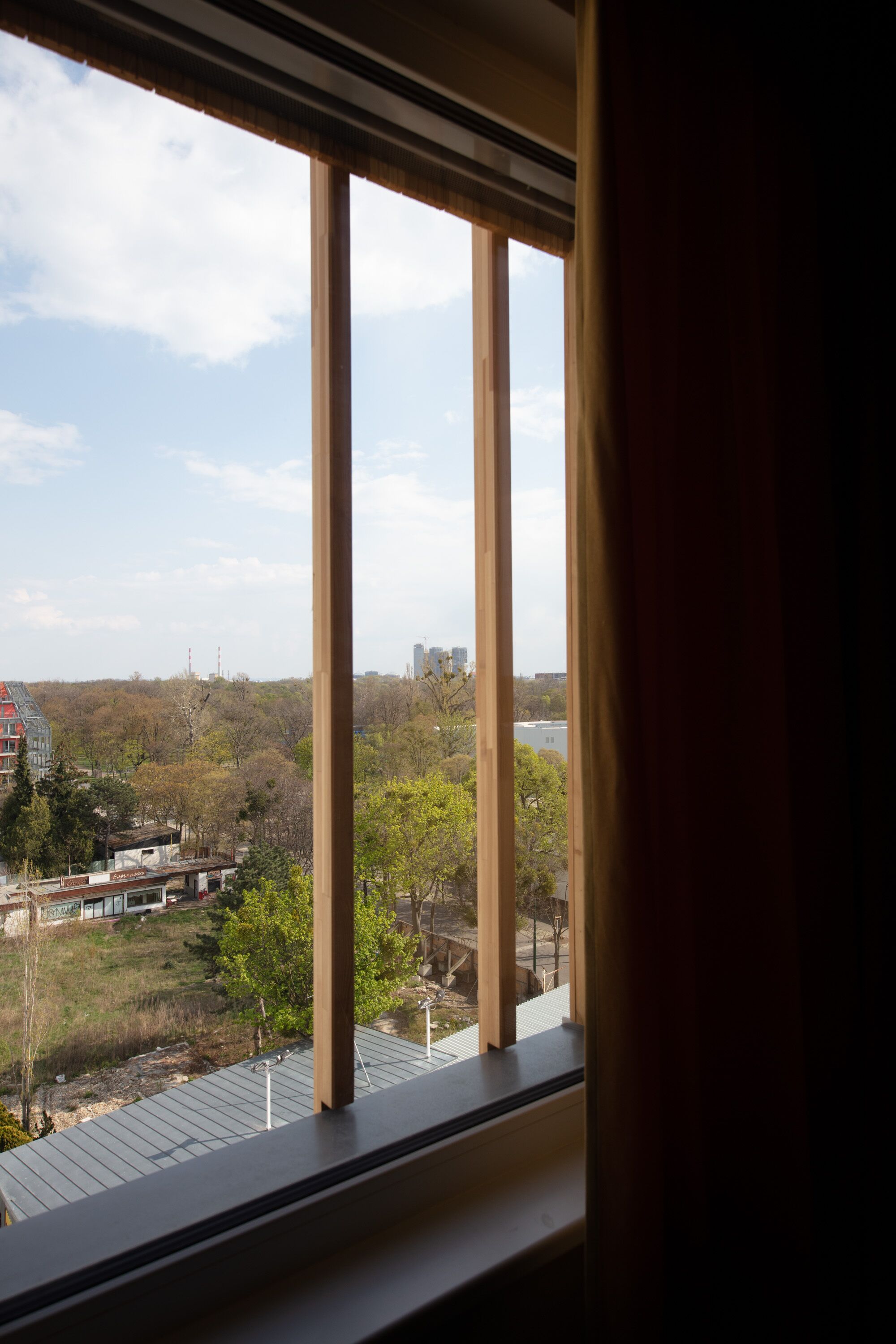 Une vue depuis une fenêtre donnant sur un parc et des bâtiments situés au loin.