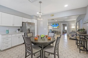A modern kitchen with white cabinets, a stainless steel refrigerator, and a dining area with a round table and chairs.