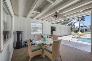 A covered outdoor dining area with wicker chairs, a glass table, and a ceiling fan. - Home on Water | Pool/Lanai Kitchen/Walk to Beach (Marco Island)