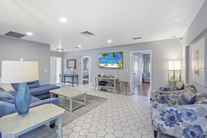 Un salon moderne avec un canapé, une table basse et un mur décoré d’une œuvre d’art représentant une scène de plage.