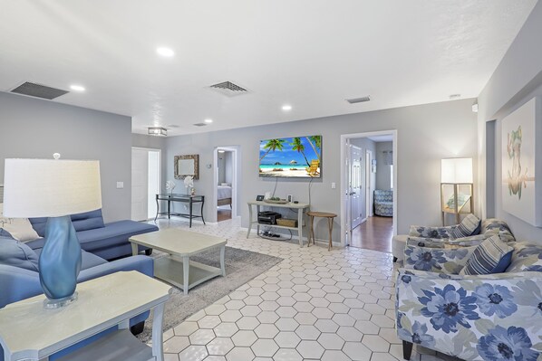 A modern living room with a sofa, coffee table, and a TV wall art depicting a beach scene.