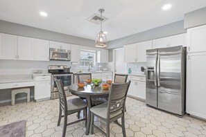 A modern kitchen with white cabinets, stainless steel appliances, and a dining area with hexagonal tiles.