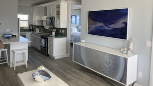 Una cocina moderna con armarios blancos, un comedor con mesa y sillas blancas, y un cuadro abstracto de gran tamaño en la pared.