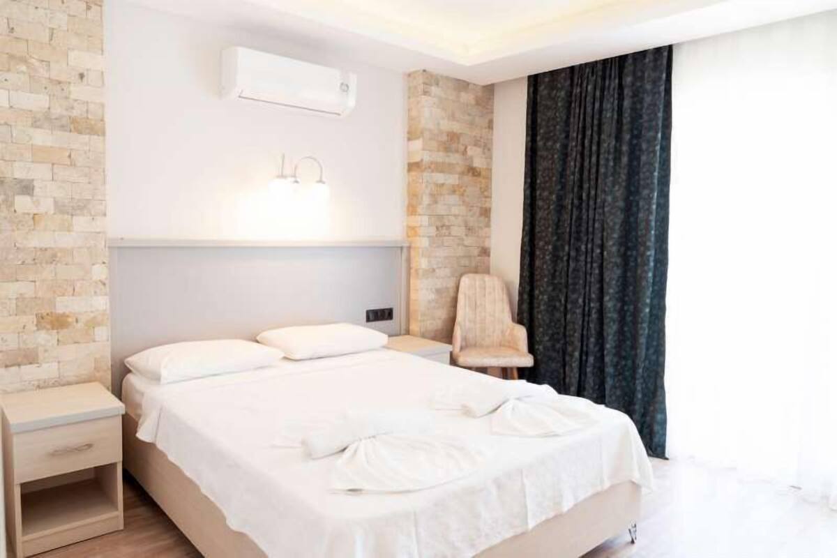 A modern hotel room with a large bed, a nightstand, a chair, and a window with curtains.