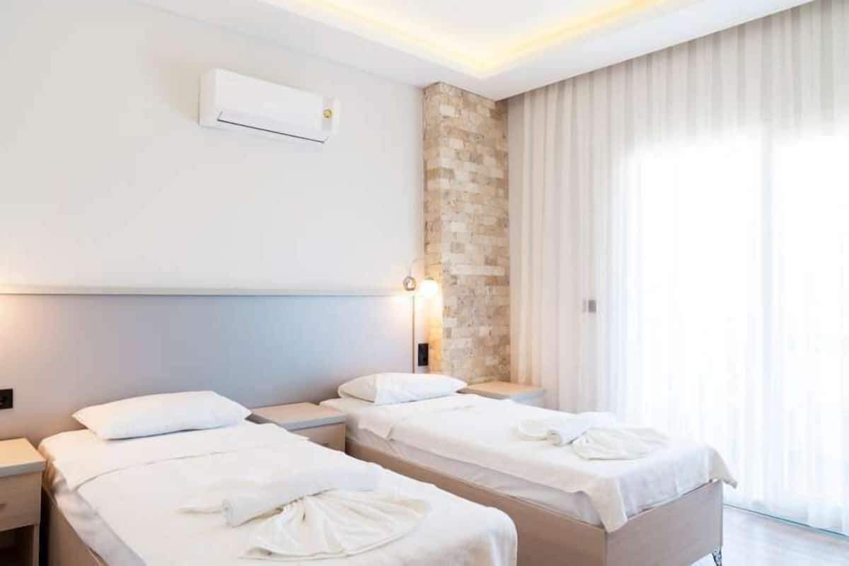 A hotel room with two beds, a stone accent wall, an air conditioning unit, and a large window with sheer curtains.