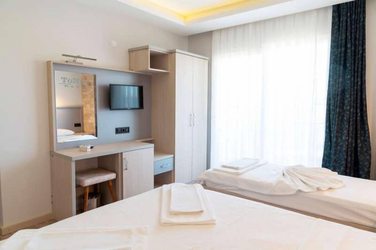 A hotel room with two beds, a desk with a TV, a wardrobe, and a window with curtains.
