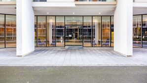 A modern hotel entrance with glass doors, a clear view of the interior, and a paved walkway leading to seating areas.