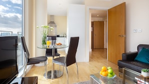 A modern living room with a glass coffee table, a black leather sofa, and a dining area with a glass table and chairs.