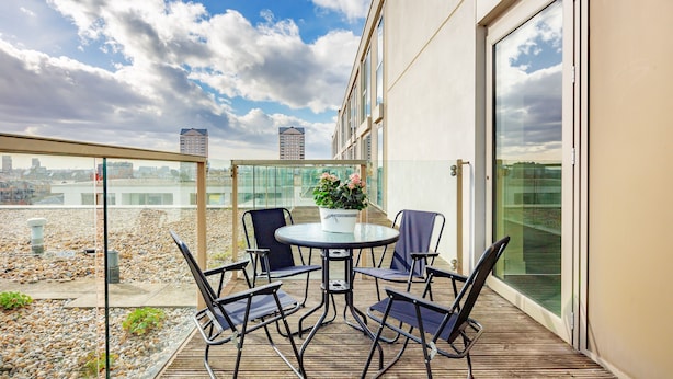 A balcony with a table and chairs, a potted plant, and a city view.