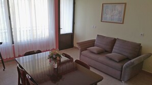 A living room with a brown sofa, a dining table with chairs, and a vase with flowers. - Apartment Kata (Lumbarda)