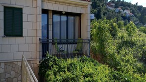 A residential building with a tiled roof, a balcony with a metal railing, and a stone facade. - Apartment Kata (Lumbarda)