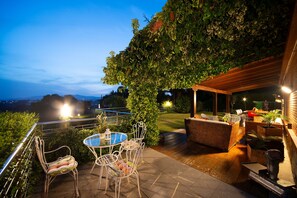 Een terras buiten met een tafel en stoelen, een houten pergola en uitzicht op het landschap.