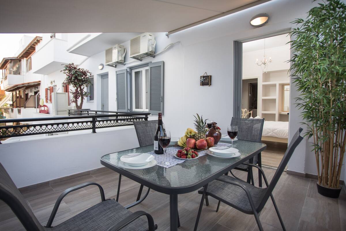 A dining area with a glass table, four chairs, and a fruit platter.