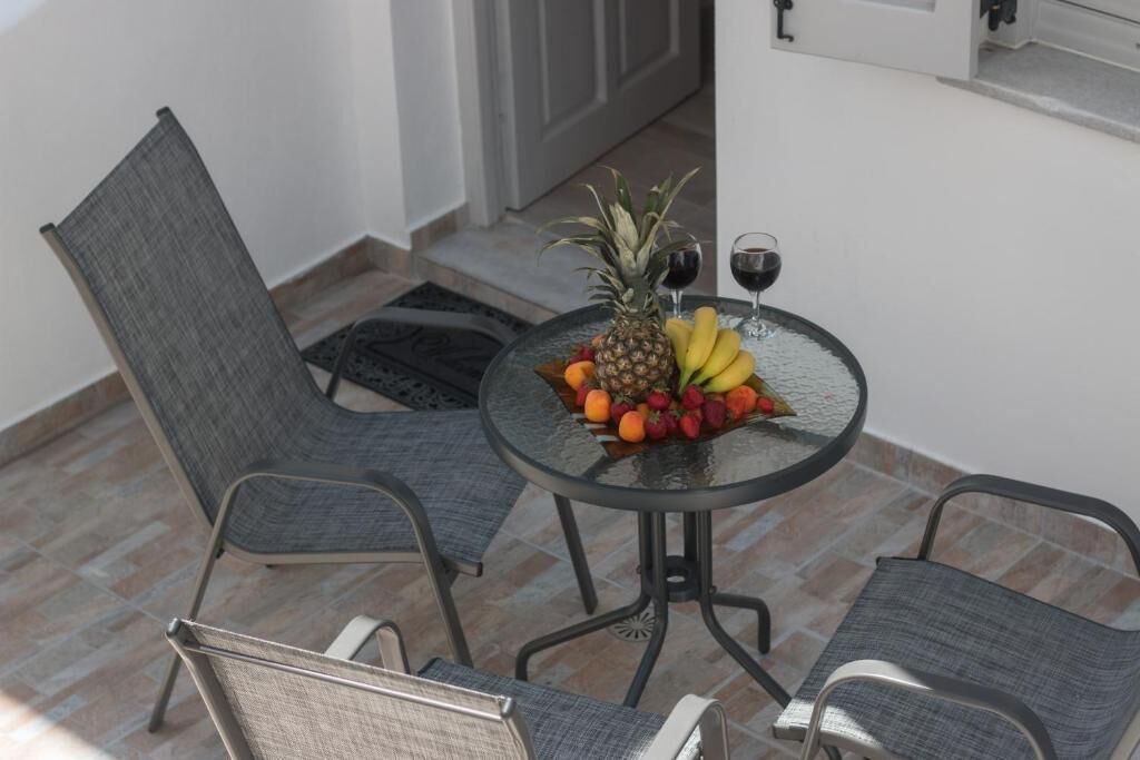 A small round table with a fruit bowl, two glasses of red wine, and two grey chairs.