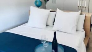 Ein ordentlich bezogenes Bett mit weißen Leinen, einem blauen Zierkissen und einer Weinflasche auf einem Tablett.