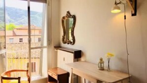 Ein Zimmer mit einem Holztisch, einem Stuhl, einem Spiegel und Blick auf Gebäude durch ein Fenster.