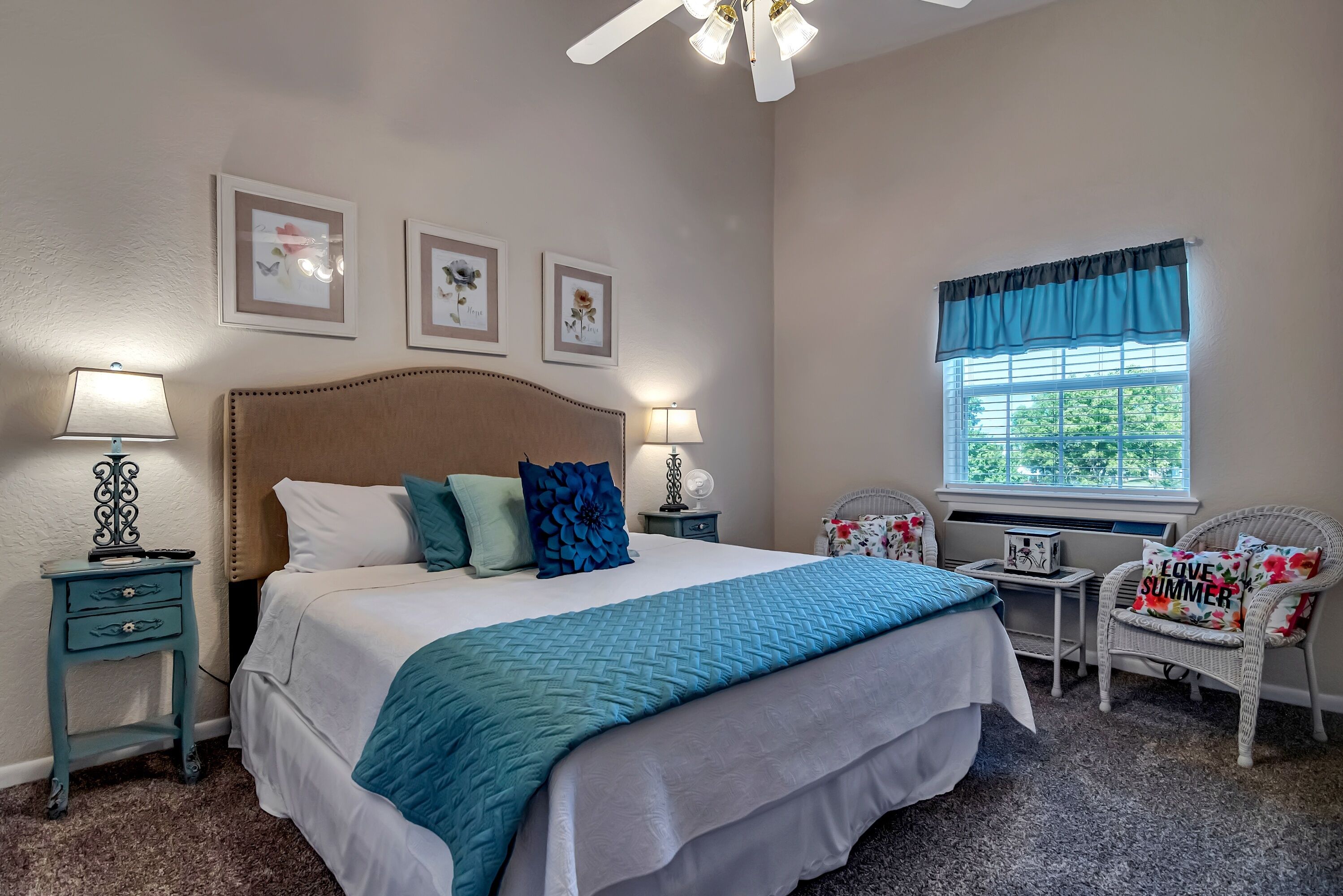 A bedroom with a bed, two bedside tables, a chair, a window with curtains, and wall art.