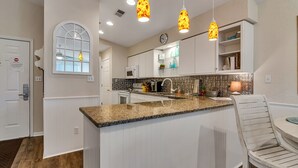 Una cocina moderna con armarios blancos, encimeras de granito e iluminación colgante.