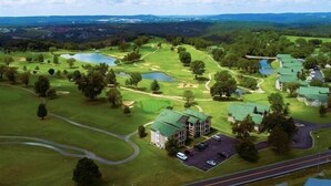 Vista aérea de un campo de golf con varios edificios, incluido un club de campo y un estacionamiento.