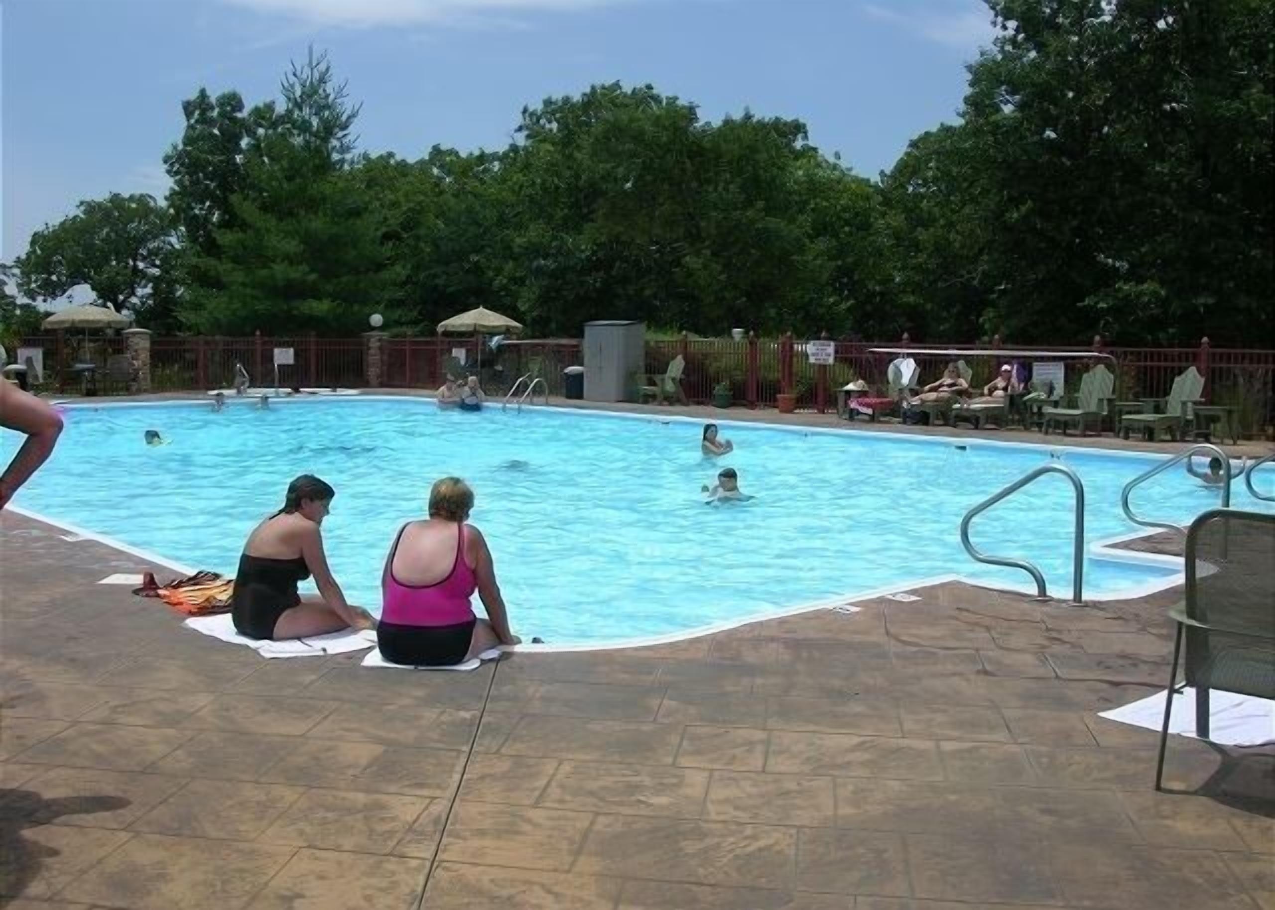 An outdoor swimming pool with people in the water and on the poolside.