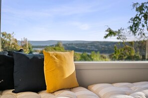 A window seat with cushions, a view of a landscape with hills and trees.