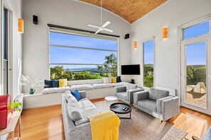 A modern living room with a large window, a ceiling fan, and a flat-screen TV.