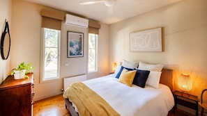 A bedroom with a bed, bedside lamp, artwork, and a window with a view.