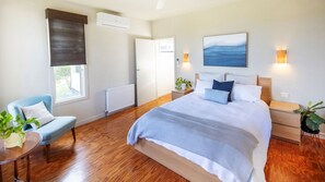A bedroom with a large bed, bedside tables, a chair, a window with a blind, and a painting on the wall.