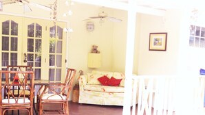 A covered patio area with a pool, wooden chairs, a sofa, and a ceiling fan.