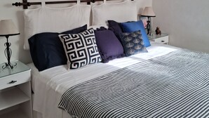 A neatly arranged bedroom with a bed, bedside tables, and a macrame wall hanging.
