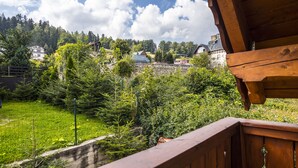 Uitzicht vanaf een houten balkon op een weelderige tuin met een stenen muur en diverse bomen.