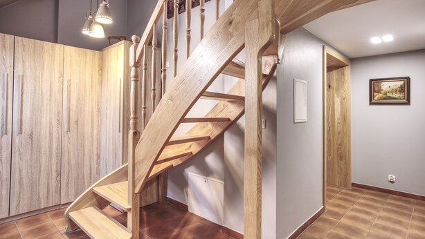 Een houten trap met een modern ontwerp, die leidt naar een kamer met een witte deur en een lijst met een afbeelding aan de muur.