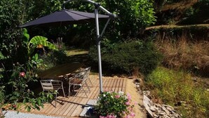 En terrasse med et bord og stole, omgivet af grus og beplantning.