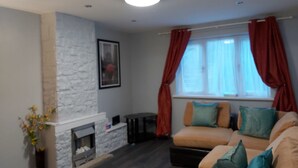 Una sala de estar con chimenea de piedra, un sofá con cojines, una ventana con cortinas y una mesita.