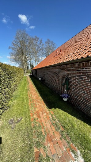 A brick building with a red-tiled roof, a brick pathway, and a hedge.