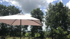 Een terras buiten met rieten meubels, een tafel en een grote parasol.