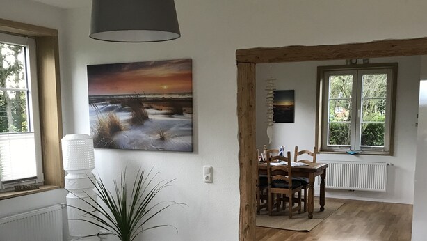 Een eetruimte met een houten tafel, stoelen, een potplant en een schilderij aan de muur.