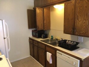 Cocina compacta con armarios de madera, microondas, tostadora y lavavajillas.
